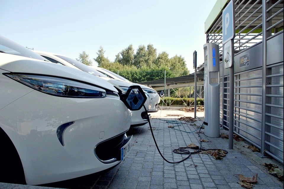 Scène extérieure urbaine avec véhicule électrique blanc en charge via câble bleu connecté au port de recharge latéral