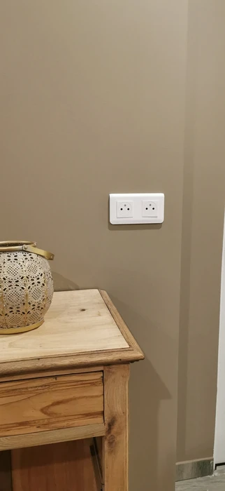 Intérieur, main tenant un tuyau d'arrosage sortant d'un mur endommagé avec débris de plâtre et éléments de plomberie apparents
